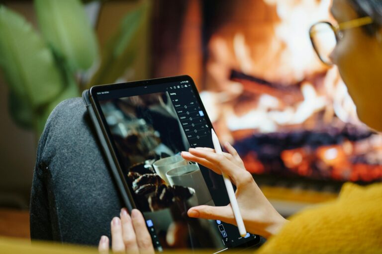 A person using a tablet for photo editing while sitting by a cozy fireplace indoors.