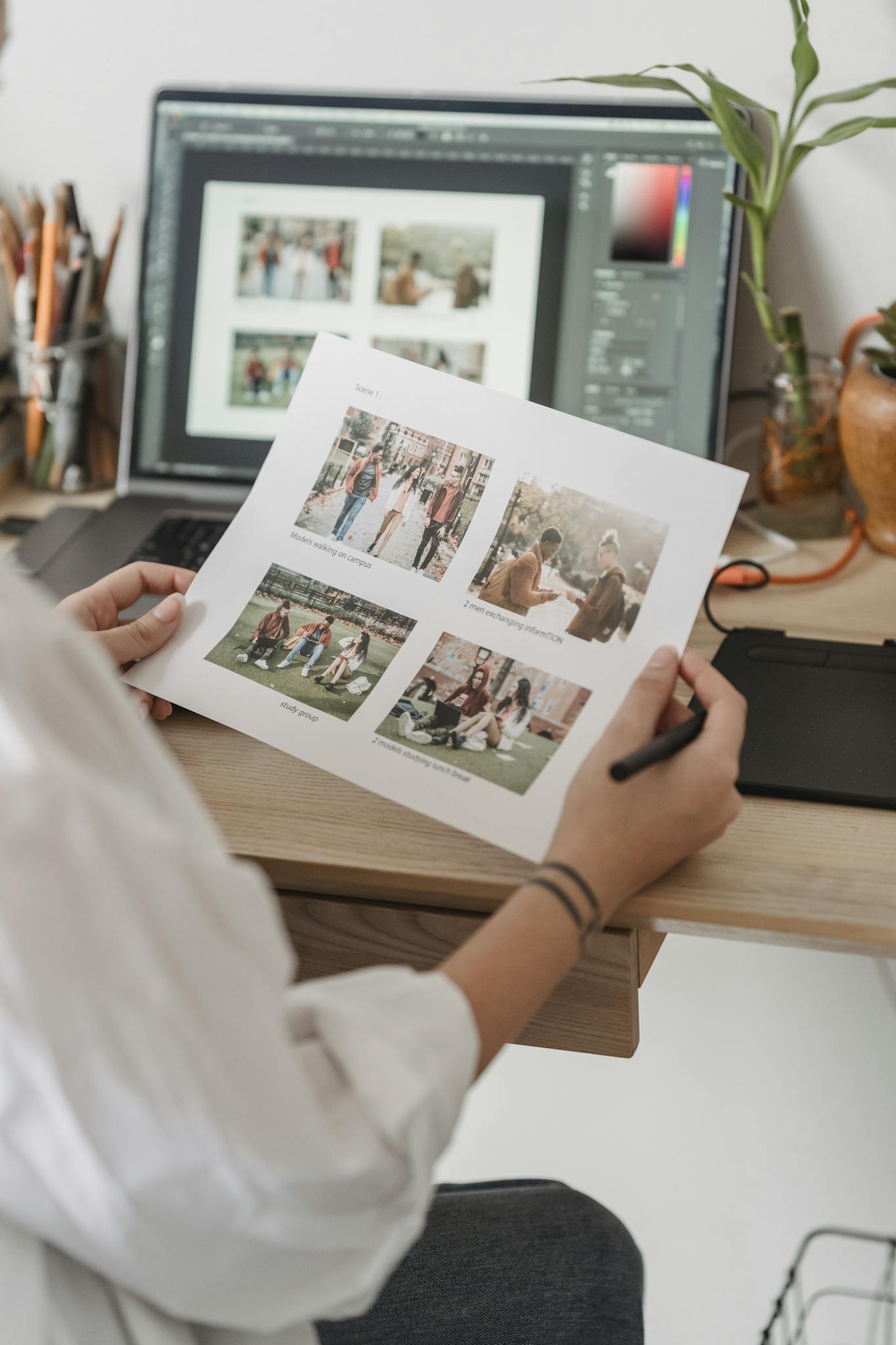 Back view high angle of unrecognizable female photographer sitting at table with netbook and looking through printed photos